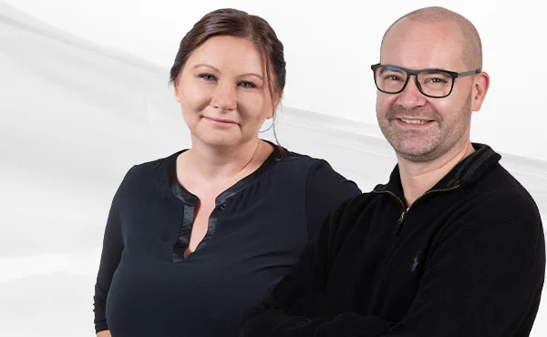 Patrycja Schrenk und Christian Heutger von PSW Training lächeln gemeinsam in die Kamera vor hellem Hintergrund.